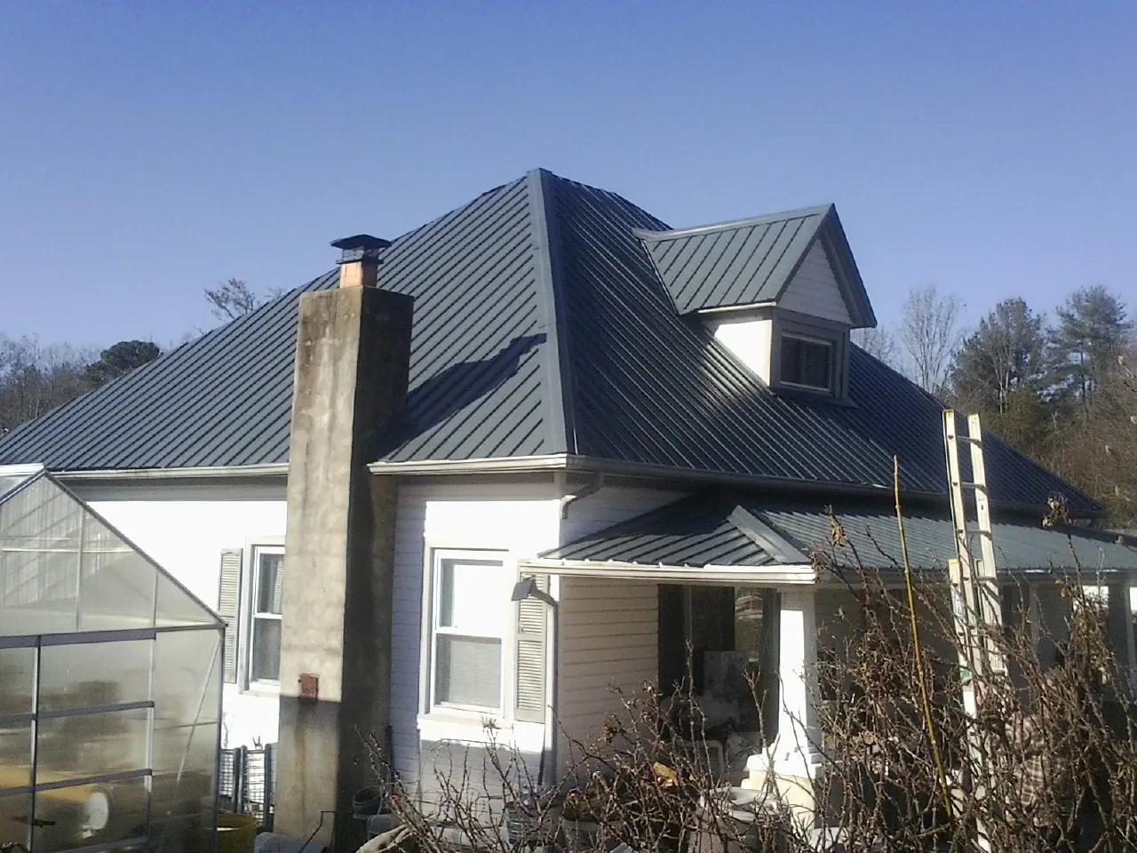 Dark blue standing seam metal roof on a white farmhouse with dormer — Slate & Tile Roof Repair by Roofing Brothers in Triangle