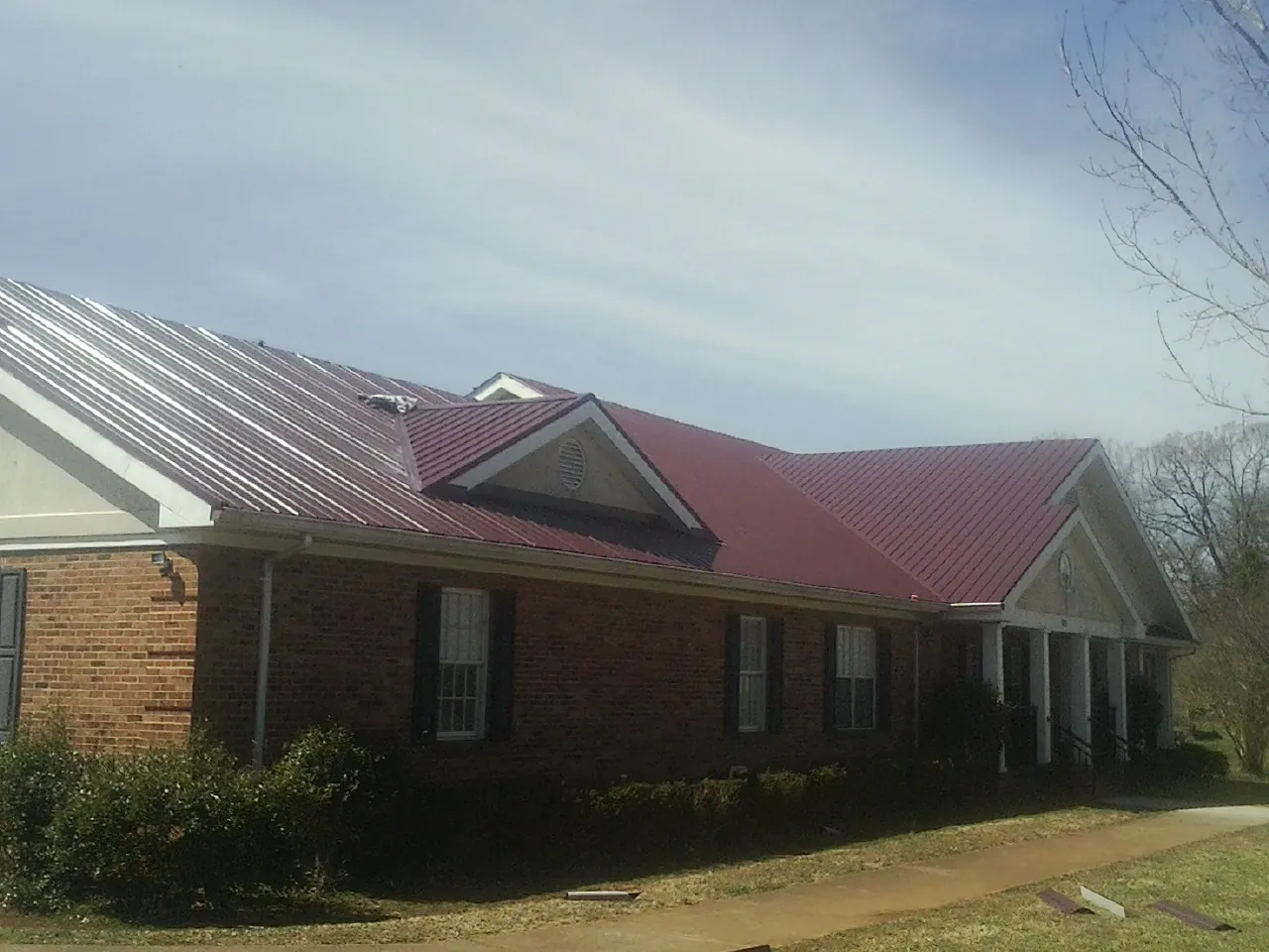 Red metal roof with gabled entries on a long brick building, from a Hail Damage Roof Repair job in Triangle