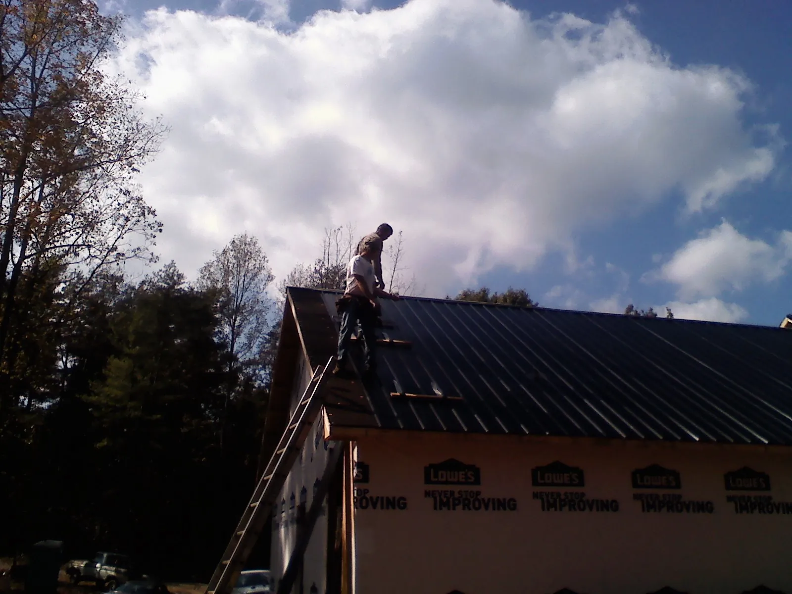 Roofer fastening dark metal panels high against a cloudy sky, from a Roof Inspection job in Triangle