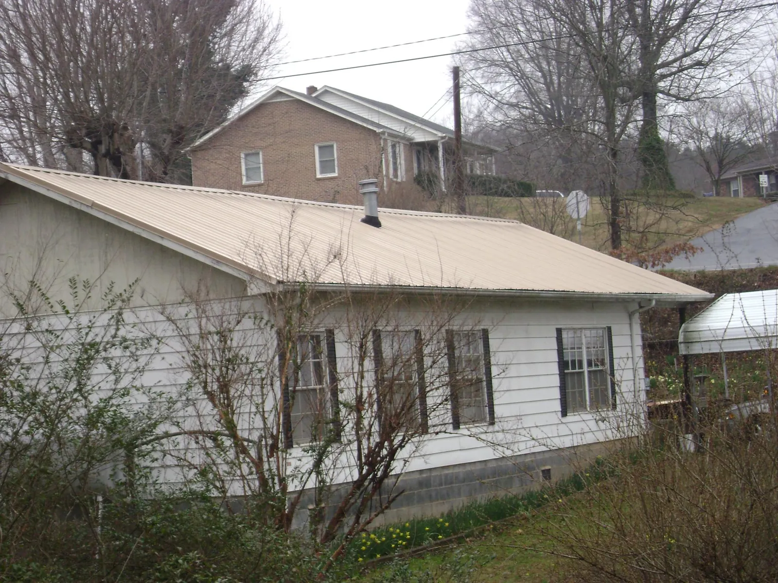 Tan metal roof on a white sided house set into a hillside — Commercial Roofing by Roofing Brothers in Triangle